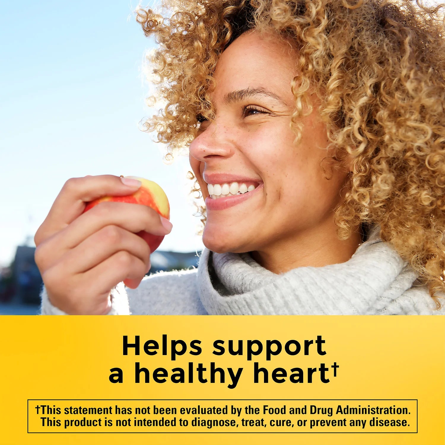 Woman holding an apple with text about supporting a healthy heart on a yellow background. Cholesterol lowering plant sterols and stanols tablets by Nature Made